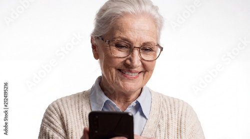 An elderly woman with glasses and a warm smile gazes at her phone, showing engagement with modern technology.