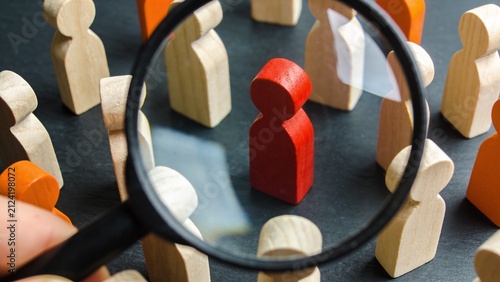 Magnifying glass focusing on red wooden figure among others with magnifying leadership selection
