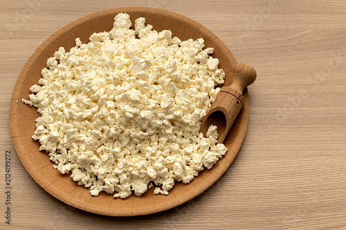 White crumbly cottage cheese on a craft plate with a wooden scoop.