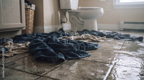 Water spills onto a tiled bathroom floor with towels scattered around and a toilet visible.