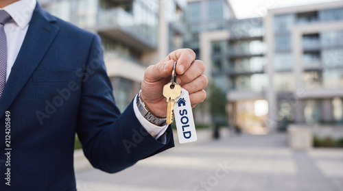 A real estate agent in a suit holds a key with a 