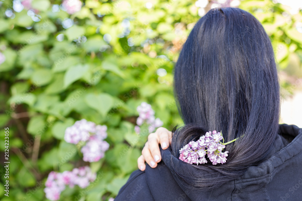 Naklejka premium Dark haired girl with lilac flowers on her hair. Rear view. Closeup.