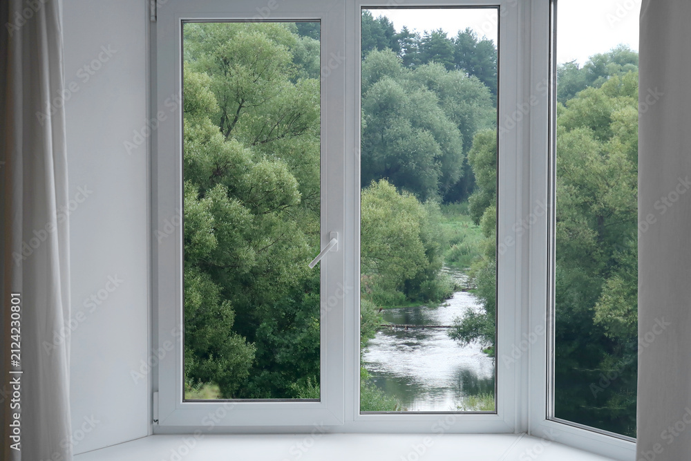 Fototapeta premium A view from the window of a landscape with green willows on the riverbank.