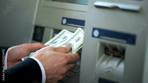 Man counting dollars withdrawn from ATM machine and putting cash in wallet for convenience and 24h banking service in 4K Ultra HD footage
