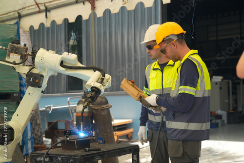Workers operate a robotic arm for welding in a factory setting during the day