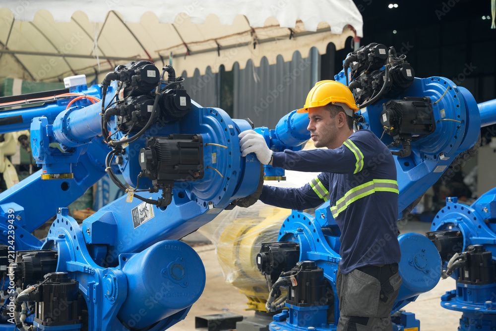 Fototapeta premium Worker in a facility adjusts robotic arm during assembly process at manufacturing site