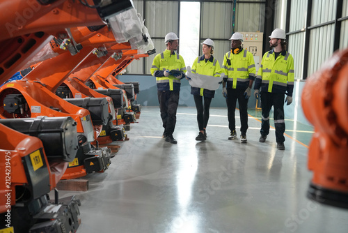 Obraz na plátně Workers review plans in a factory with robotic arms for assembly on a weekday mo