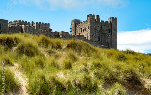 Historic medieval castle set among sand dunes on the North East coast, dramatic coastal setting with weathered stone architecture against shifting sands and sky.