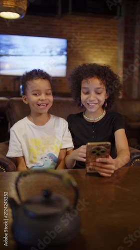 Black sister showing smartphone to younger brother