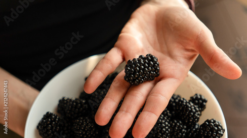 Hands holding a white bowl filled with fresh ripe blackberries, close-up shot.