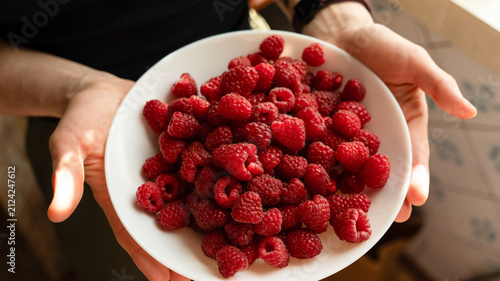Fresh ripe raspberries piled high in a white ceramic bowl on a light marble tabletop, top down view.