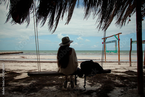 фотографія Woman relaxing on a wooden swing under a thatched roof palapa looking at the ocean