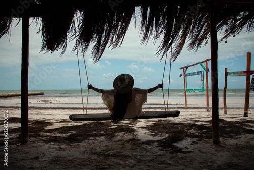 Photography Woman relaxing on a wooden swing under a thatched roof palapa looking at the ocean