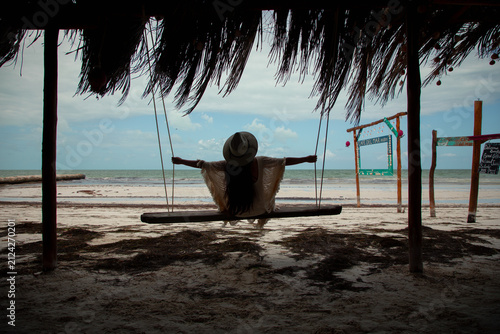 Canvas Print Woman relaxing on a wooden swing under a thatched roof palapa looking at the ocean