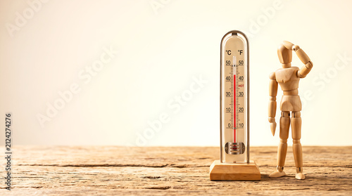 Heat wave climate change concept with wooden figure wiping sweat near high temperature thermometer and copy space for presentation banner
