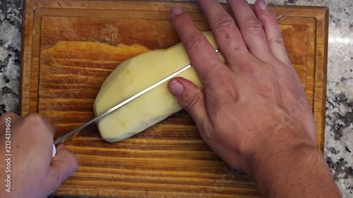 Mano de cocinero cortando papa pelada sobre tabla de madera