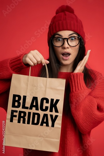 Surprised young woman in red winter clothing holding a shopping bag for black friday sales event