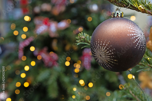 Close-up of matte dark brown Christmas tree ball toy with silver pattern on fir branch against background of blurred garlands. Background for postcards and greetings