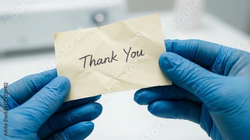 Gratitude message with thank you note held by hands wearing blue protective gloves closeup 
