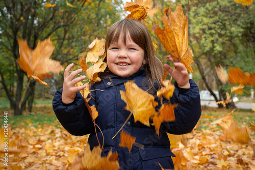 Joyful child playing with golden maple leaves in autumn park. Motion blur