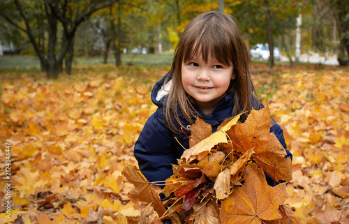 Joyful child playing with falling yellow leaves, autumn background