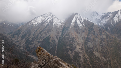 Towering mountains stretch towards a grey sky, their peaks adorned with patches of snow. This Pamir region captures the essence of rugged beauty, inviting adventurous hikers to explore its vastness.