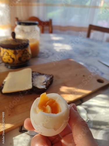 Hard-boiled egg with bright yellow yolk on a rustic breakfast table at a countryside veranda at morning.Cheese is at background 