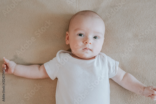 portrait of cute 2 month baby boy lying on beige blanket. Funny playful and energetic child. Babycare and safety