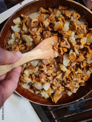 Chanterelle mushrooms, potato and onion frying in a pan while a female hand stirs with a wooden spatula,recipe,taste.Russia,Luga