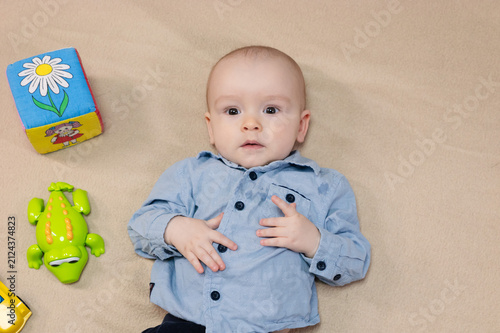 Cute 10 month baby boy lying among various playful colorful toys on beige blanket. Infant surrounded by vivid objects participating actively in sensory exploration and learning. 