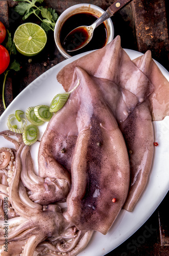 фотографія Fresh raw seafood squid or calamary and ingredients on dark background