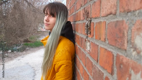 Offended teen by brick wall. A view of offended young girl stand in loneliness by the brick wall in the day light. A concept of teens problems during childhood