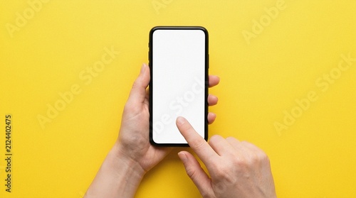 Person holding phone with blank screen, touching display on yellow background