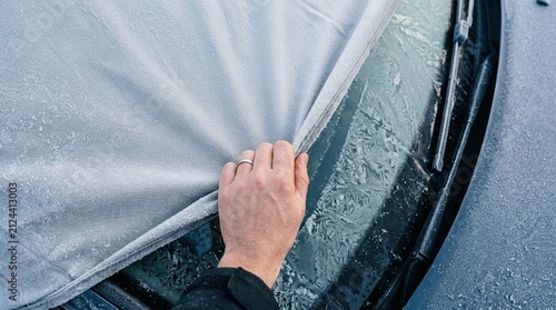 Person removing frost cover from a frozen car windshield on a cold winter morning, vehicle maintenance concept