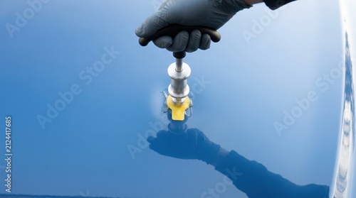 Paintless dent repair on a blue car door using a puller tool and glue tab by a mechanic in gloves