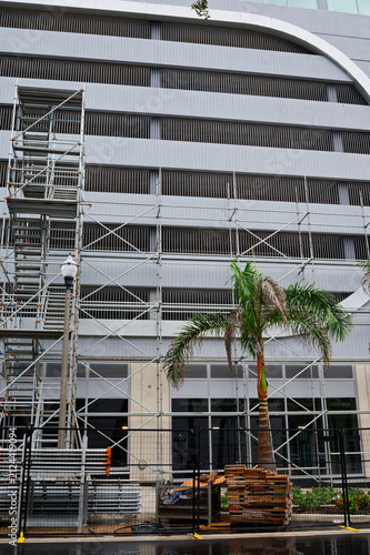Photography Scaffolding and construction materials line a downtown building frontage flanked by palm trees, wet pavement and reflective puddles after rain, conveying urban renovation and temporary disruption