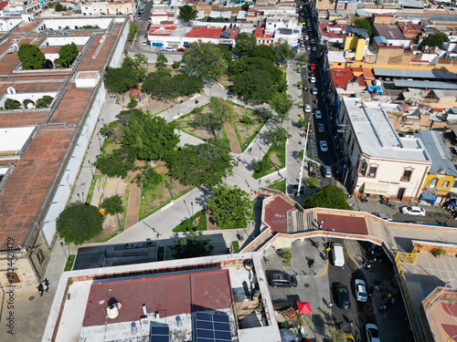 High angle drone view of Cabanas Garden, a green urban park surrounded by historic buildings and busy streets in Guadalajara, Mexico.