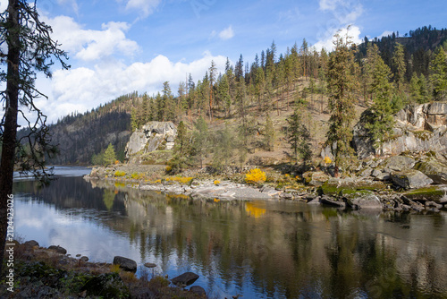 beautiful scenic photo of reflections of fall color foliage in the Clearwater River near Orofino Idaho featuring a rocky beach and a bluff