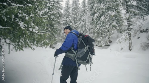 Hiker in blue jacket walks through snowy forest using poles for winter hiking