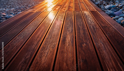 dark wooden deck planks laid on colorful pebbles golden hour light