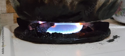 Close up of a blue gas flame burning under a dark pot.