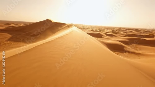 Golden sunlight illuminating rolling sand dunes in a vast desert landscape at sunset with wind blowing