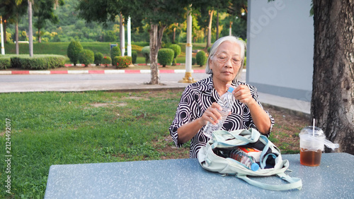 Happy Asian senior woman sitting alone outdoors at cafe table. Retirement freedom and relaxed elderly lifestyle concept.