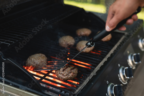 Person checking homemade beef burger patties with a digital meat thermometer on a hot gas grill