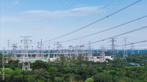 фотографія An outdoor high voltage power substation with multiple transmission towers and power lines, surrounded by green vegetation under a clear sky