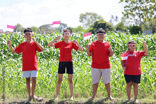 Photography Photo of four children standing in a row in a rice field while carrying the Indonesian flag, smiling at the camera