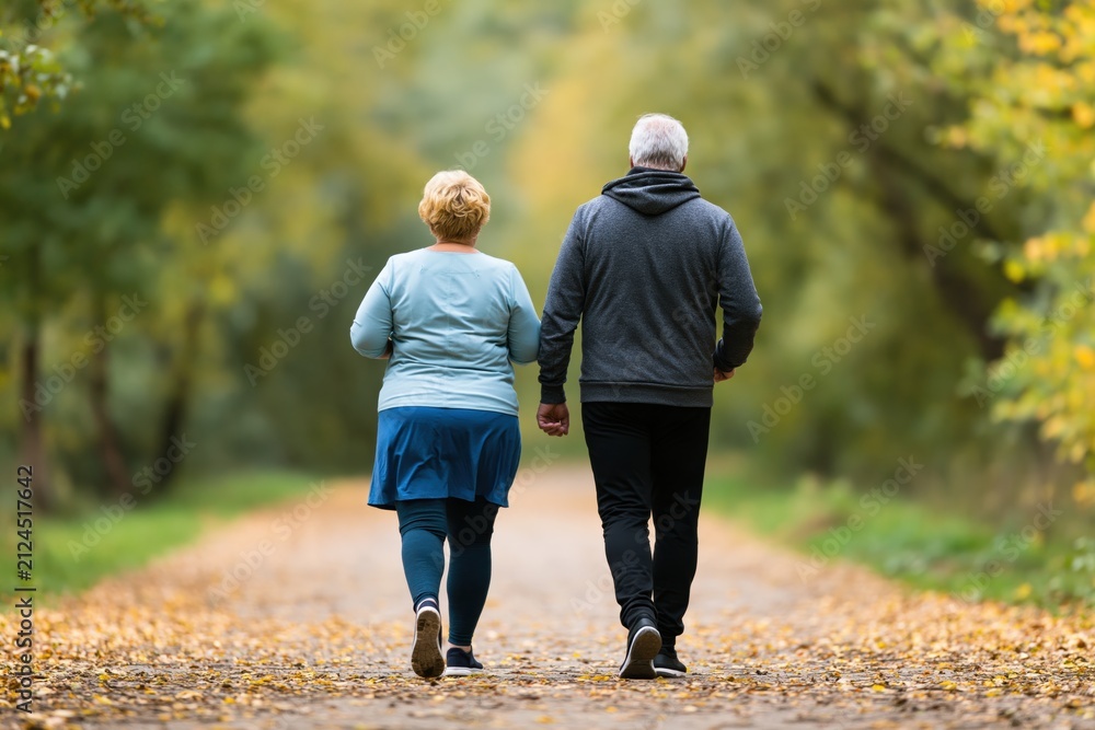 Obraz premium Senior couple walking together on a path in an active autumn forest park outdoors