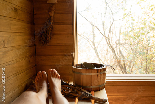 Quadro su tela Feet rest on wooden bench in cozy sauna while sunlight filters through quiet win