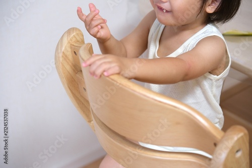Smiling toddler holding the back of a wooden chair
