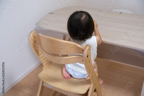 Back view of a toddler wearing a diaper sitting on a wooden chair at a table